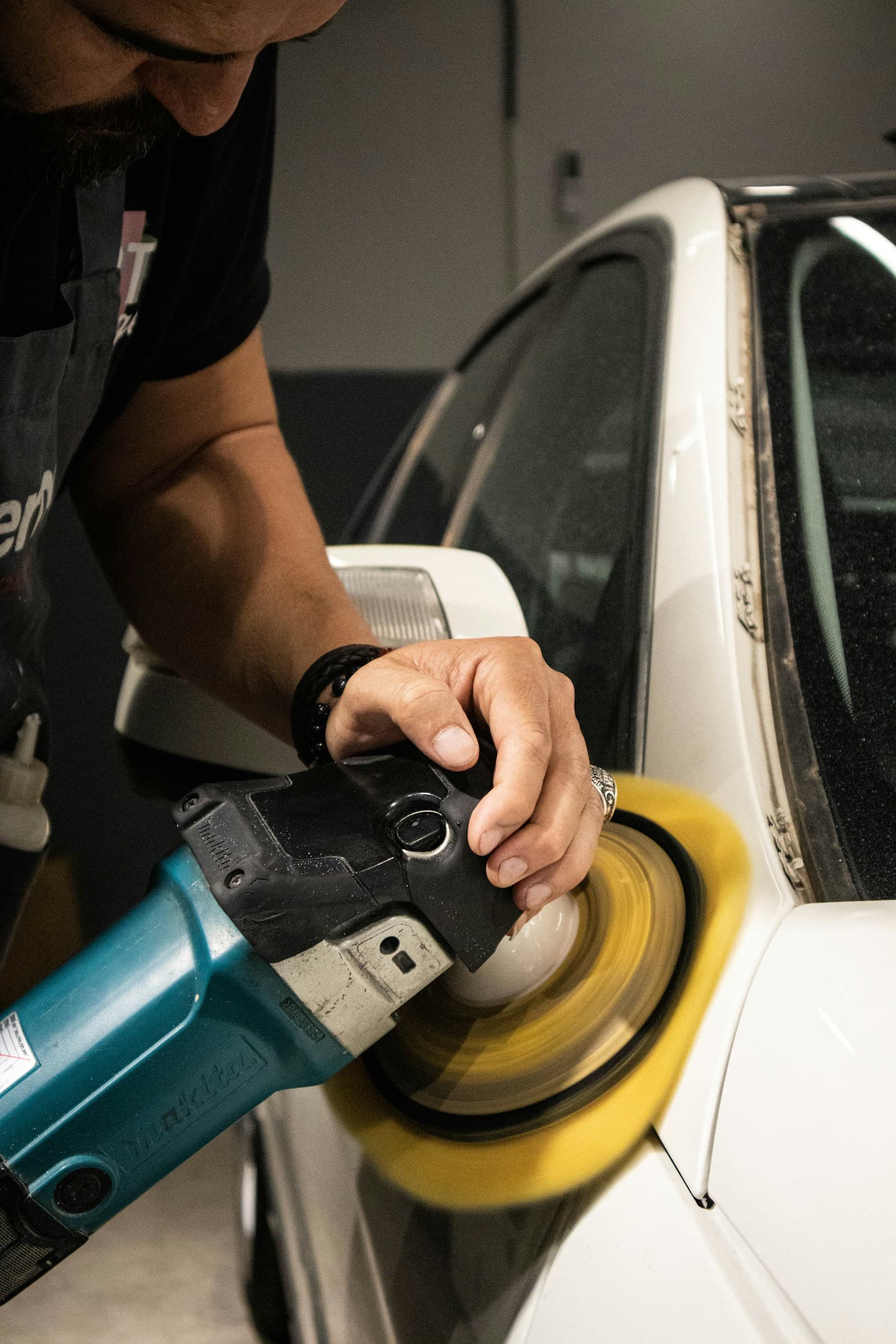 A detailer machine-polishing a white car.